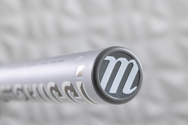 Close-up of the 2025 Marucci Echo DMND2 (-9) Fastpitch Softball Bat (MFPED29) end cap shows a white "M" logo on gray, with a blurred white background and Marucciβs innovative liquid-gel knob design.