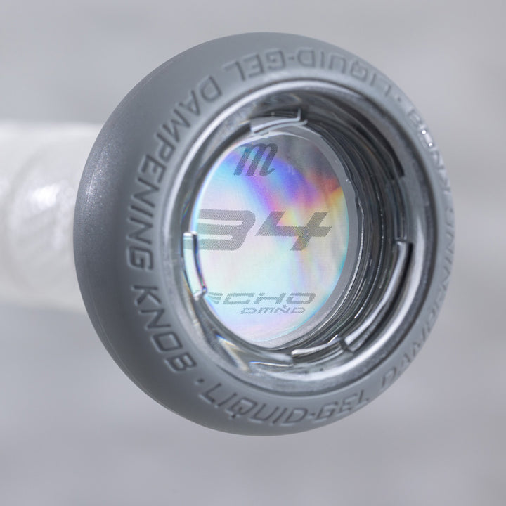 Close-up of a round, gray liquid-gel knob with "LIQUID-GEL DAMPENING KNOB" text and a holographic label showing 34 and stylized textβdesigned for the Marucci 2025 Echo DMND2 (-9) Fastpitch Softball Bat: MFPED29.