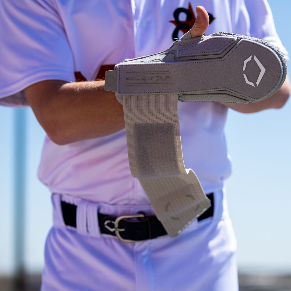 A baseball player secures the EvoShield Sliding Mitt 2.0: WB57537 by EvoShield on their left forearm for hand protection under bright daylight.