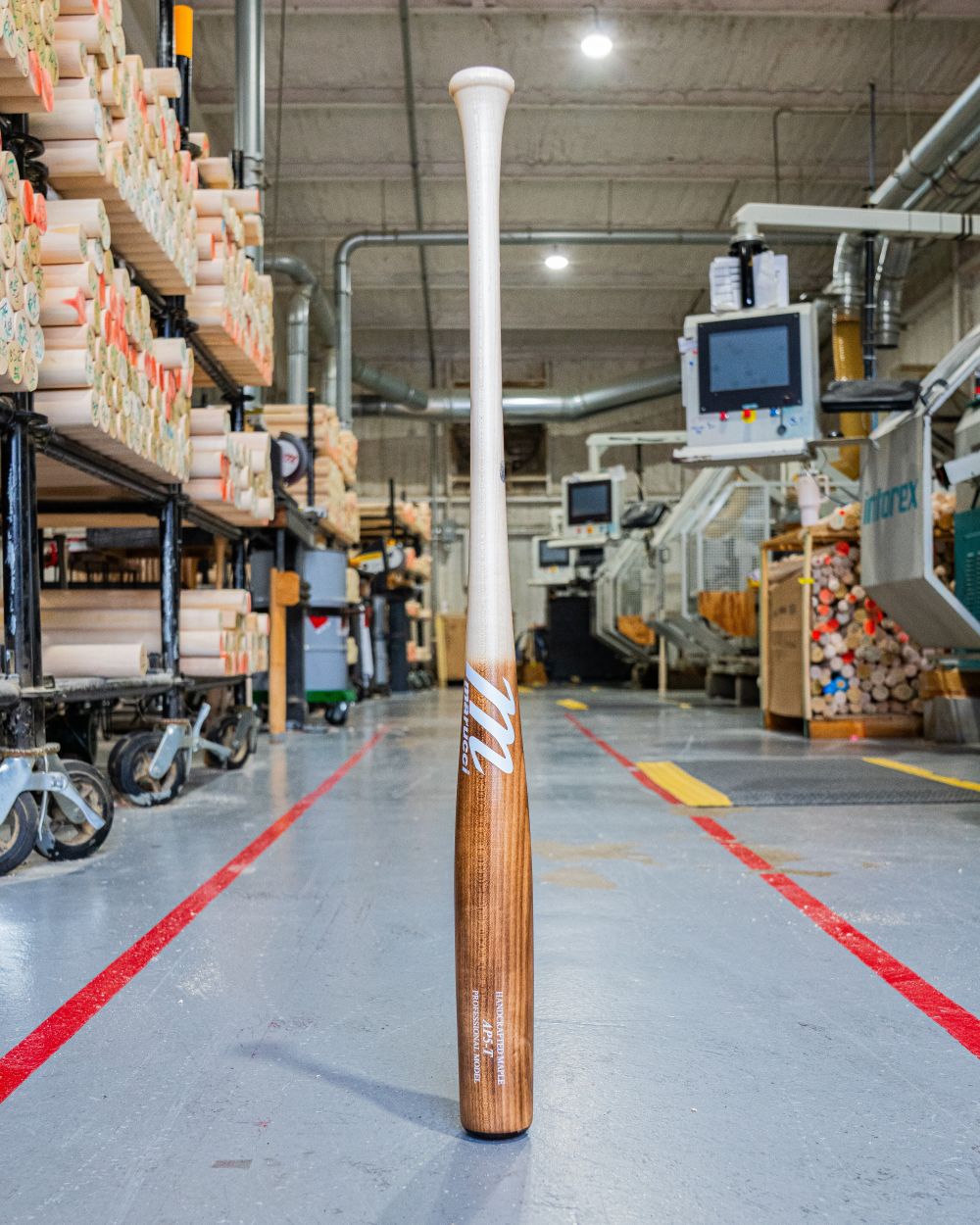 A Marucci AP5 Torpedo Pro Model Maple Wood Bat: MVE5AP5T stands upright on the factory floor, surrounded by machinery and stacks of wood—ideal for power hitters who demand quality from Marucci. Bright lights shine on polished concrete floors.