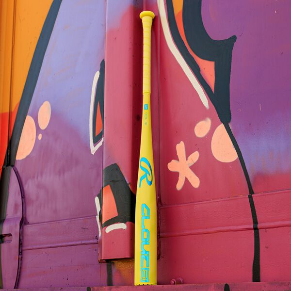 A vivid yellow 2026 Rawlings Clout AI (-3) BBCOR Baseball Bat (RBB6C3) with blue lettering stands against a purple and orange graffiti wall.