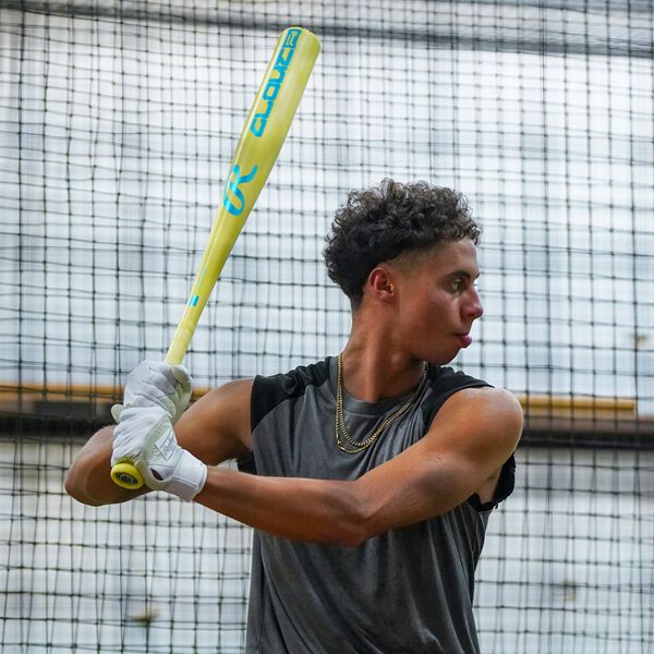 A young man in a sleeveless shirt and gloves grips a yellow 2026 Rawlings Clout AI (-3) BBCOR Baseball Bat (RBB6C3), getting ready to swing in an indoor batting cage with a netted background.