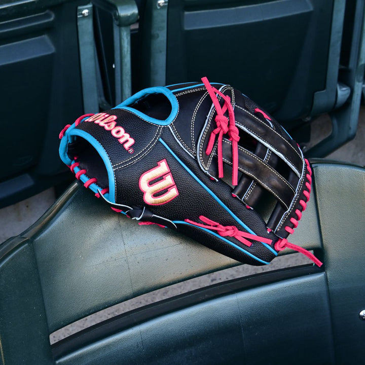 A Wilson A2000 1777SS 12.75" Baseball Glove (WBW1032221275) in black with SuperSkin, red and blue laces rests on a green stadium seat, empty seats in the background.