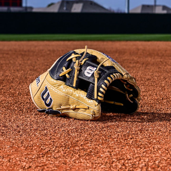 A Wilson A2000 KBH13 11.75" Ke'Bryan Hayes GM Baseball Glove (WBW1032961175) rests on the infield dirt, with green grass and a dark fence in the background.