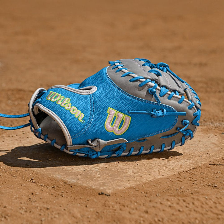 A Wilson A2000 FPCM23 34" Fastpitch Catcher's Mitt (WBW10349134) in blue and gray with light blue laces rests on the dirt at home plate.