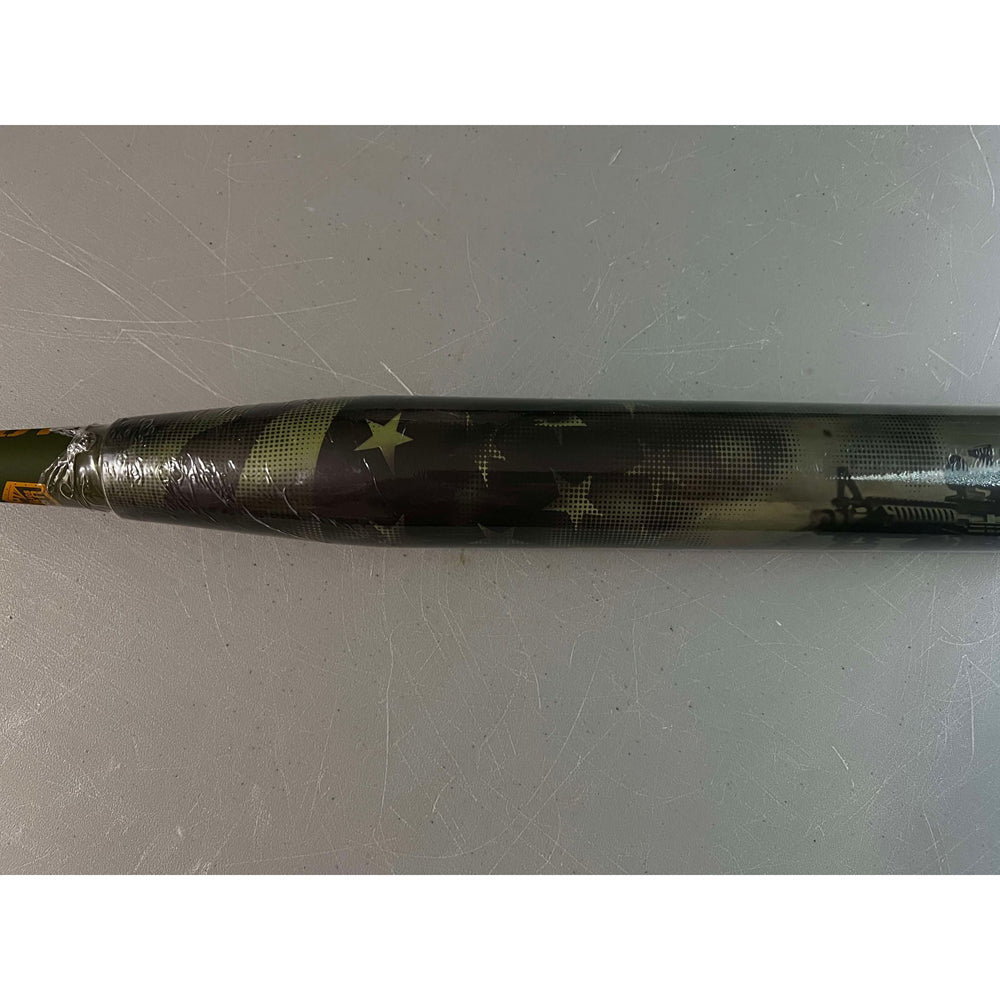 A close-up of the 2025 Pure Sports Hellfire X22 13″ Endload USA Slowpitch Softball Bat (5135M565), wrapped in plastic with a dark, star-studded, camouflage pattern, resting on a scratched gray surface.