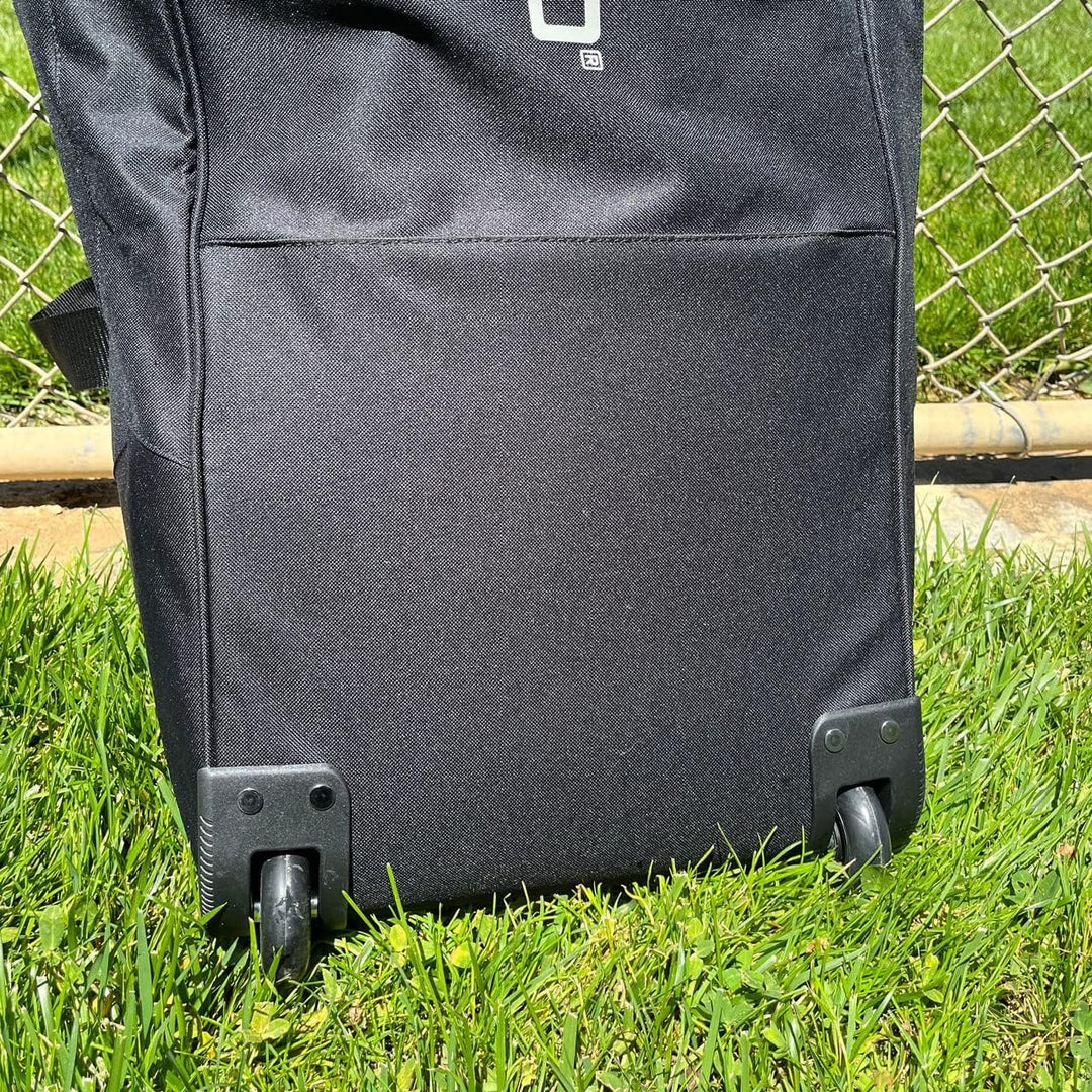 A close-up of the Champro Boss Wheeled Catcher's Bag: E92 by Champro Sports, showing two small all-terrain wheels on grass with a chain-link fence in the background.