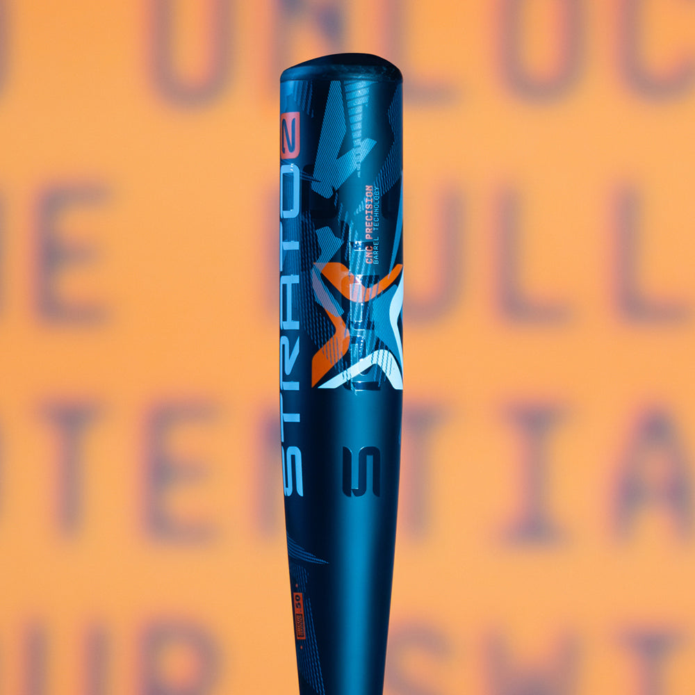 A close-up image of a dark blue baseball bat labeled STRATOZ with a stylized S and orange-gray accents, set against a blurry orange background with indistinct blue text.