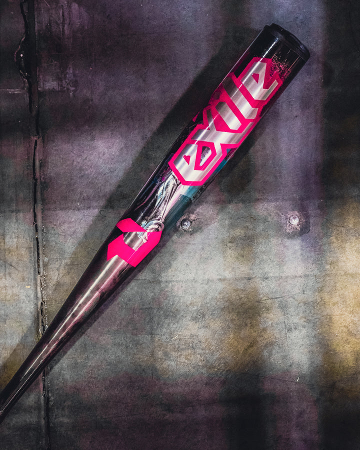 The 2026 DeMarini Exile Cyborg (-3) BBCOR Baseball Bat (WBD2654010) rests diagonally on worn concrete, featuring metallic design, bold pink Exile lettering, and an X14 Alloy Barrel for serious players.
