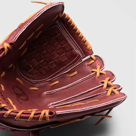 A close-up of an open maroon leather baseball glove with tan laces, showing detailed stitching and a woven pocket, set against a plain light gray background.