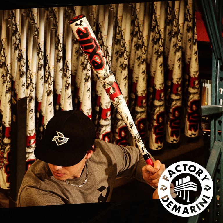 Wearing a black cap and gray shirt, a person readies to swing the 2026 DeMarini Exile (-3) BBCOR Baseball Bat: WBD2589010 by DeMarini, surrounded by bat racks and a Factory DeMarini logo in the corner.
