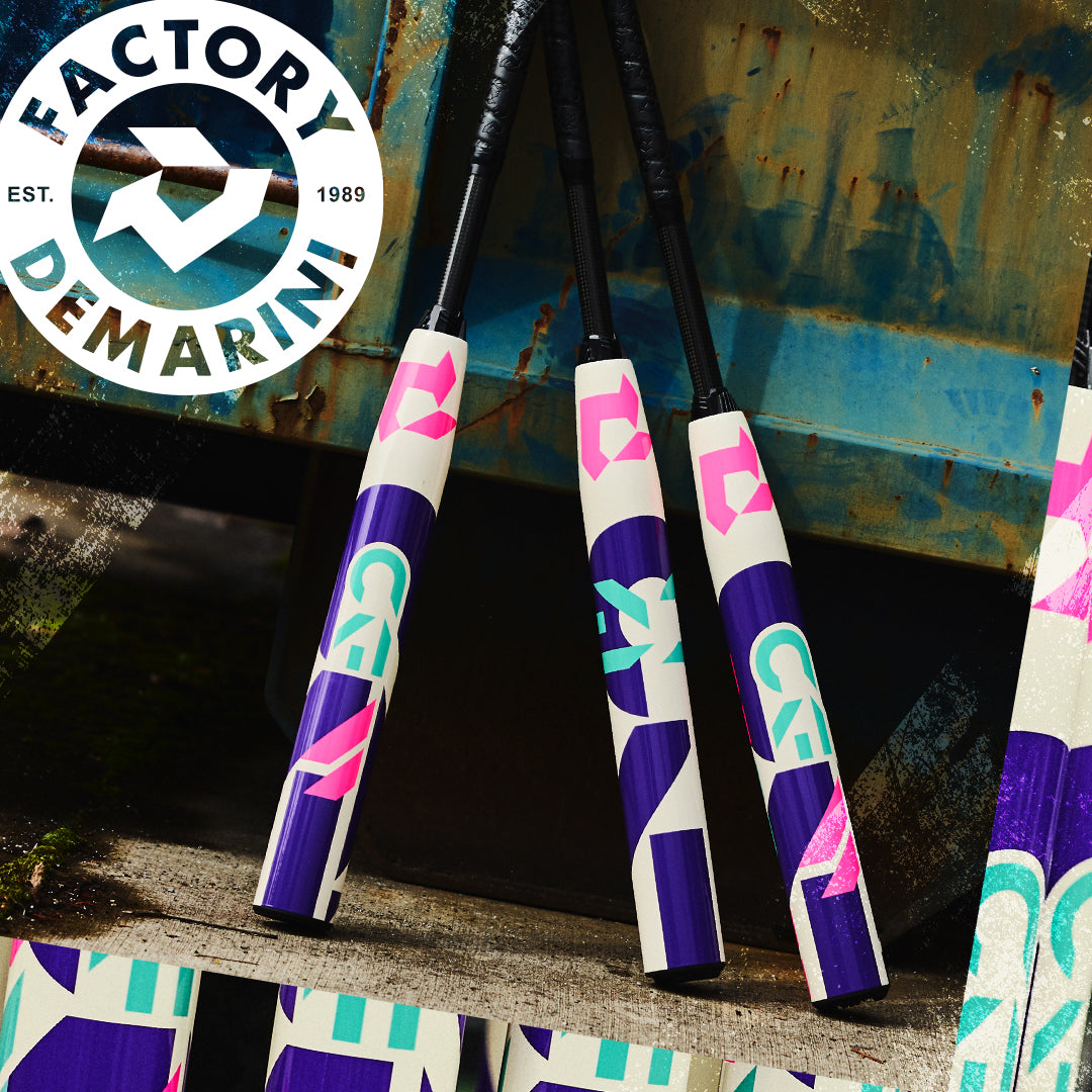 Three vibrant DeMarini 2026 CF (-11) Fastpitch Softball Bats (WBD2630010), with purple, teal, and pink geometric designs, lean against a weathered metal surface. A circular "FACTORY DEMARINI" logo appears at the top left.
