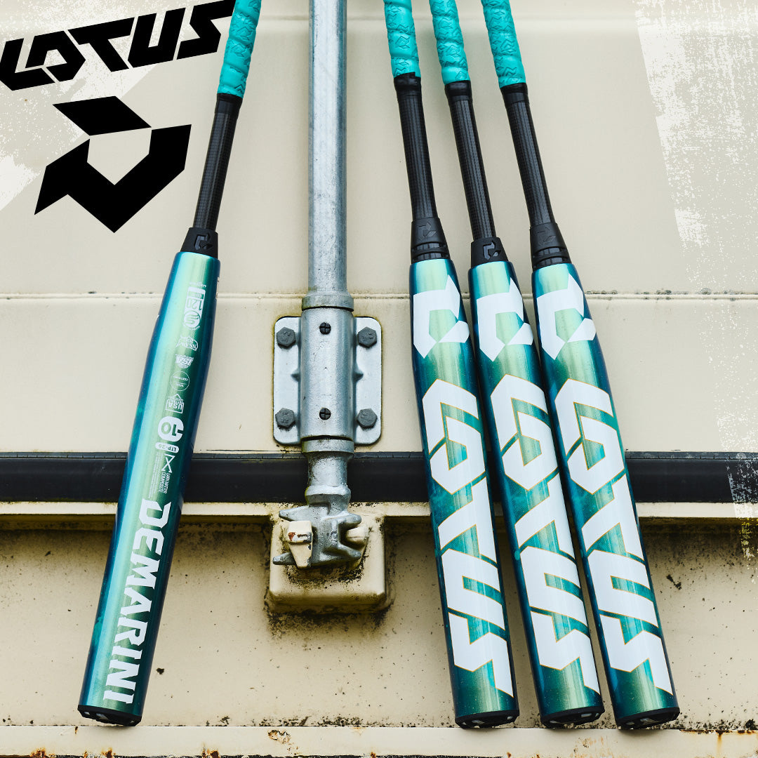 Four teal and black DeMarini Lotus softball bats are leaning against a light-colored wall with a metal pipe and hinge. Two black and white logos are visible in the upper left corner.