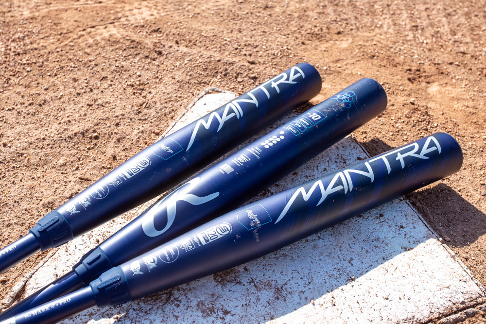 Three blue Rawlings bats labeled MANTRA lie on home plate, sunlight reflecting off the 2025 Rawlings Mantra (-9) Fastpitch Softball Bat: RFP4M9 (DEMO), built with In/Tense Carbon Composite.
