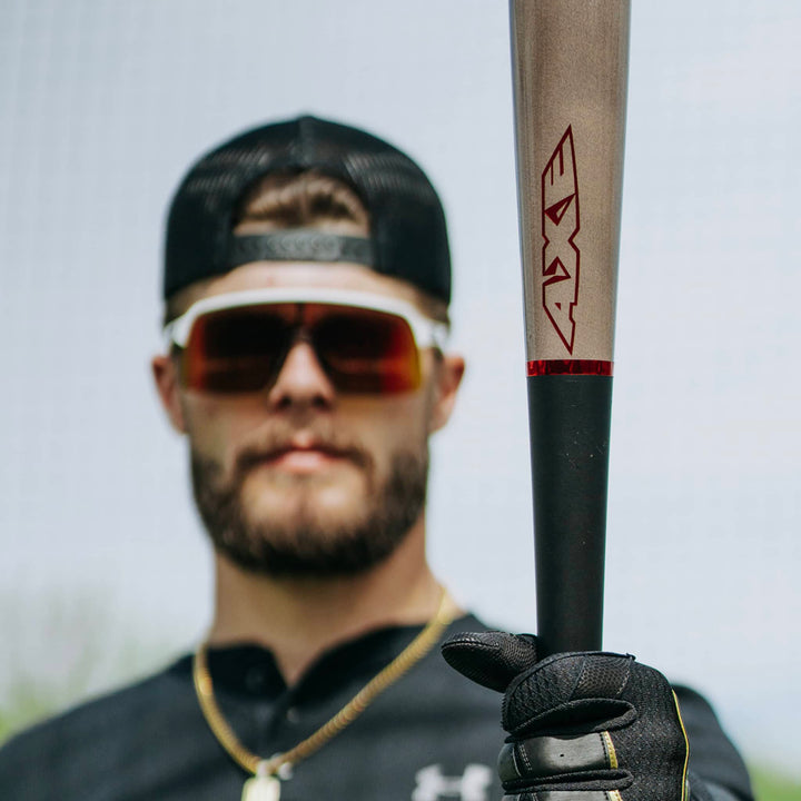 A man in sunglasses, a black cap, and gloves holds the AXE Flared Pro Series Maple Wood Baseball Bat (L124K-FLR) toward the camera; his face is out of focus and partly hidden.