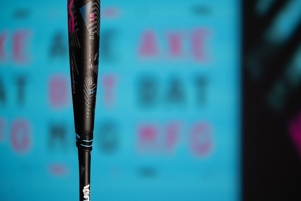 Close-up of the 2024 AXE Avenge Pro 3 Hybrid (-8) USA Baseball Bat (L174M) with blue and pink accents, set against a blurred blue background with pink and dark lettering.