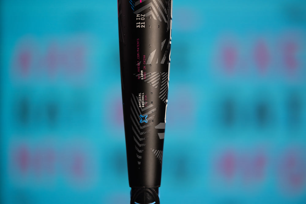 Close-up of the 2024 AXE Avenge Pro 3 Hybrid (-8) 2 5/8" USA Baseball Bat (L174M) by AXE, featuring white and pink geometric patterns and text on a blue background with blurred writing.