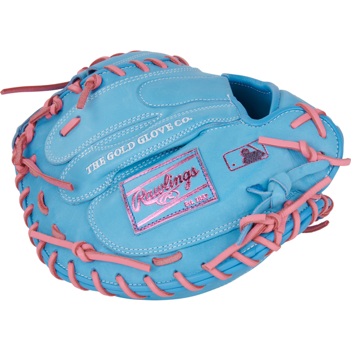 The Rawlings Heart of the Hide 33" catcher's mitt (PRORCM33-23CBP) is light blue with pink laces, stitching, and a pink Rawlings logo patch. It features "THE GOLD GLOVE CO." stamped on the outer side.