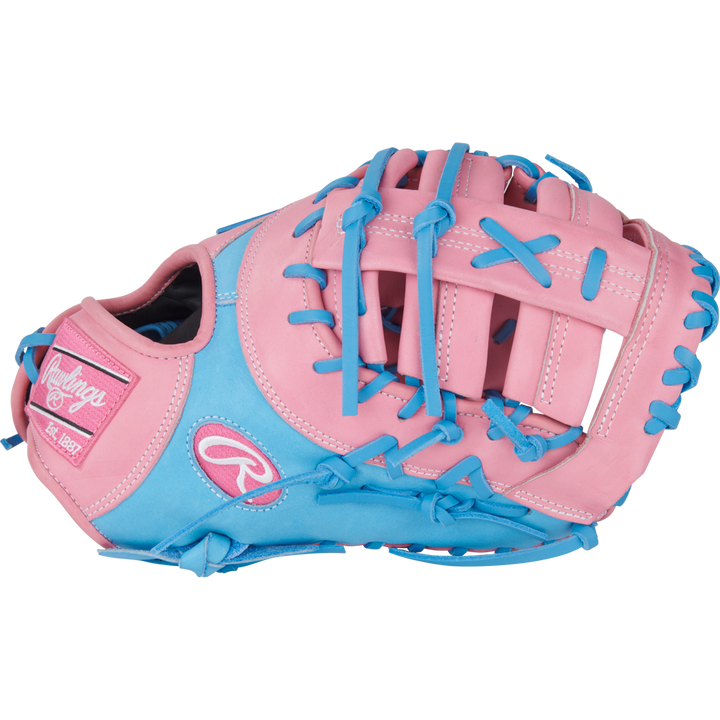 The Rawlings Heart of the Hide 12.25" First Base Mitt (PRORDCTU-10PCB) features a pink and light blue design with blue laces, pink patches, ContoUR Fit, and bold Rawlings branding on the thumb.