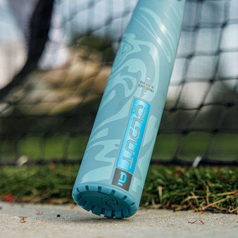 A close-up of the barrel end of a light blue 2025 Rawlings Clout AI (-3) BBCOR Baseball Bat: RBB5C3 (USED) with "CLOUT" visible, resting on concrete by artificial turf and a black net in the background.
