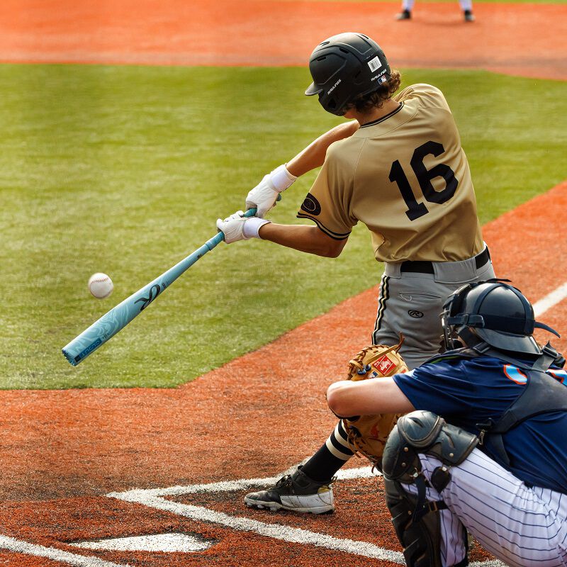 A baseball player in a tan jersey with #16 swings a 2025 Rawlings Clout AI (-3) BBCOR Baseball Bat (USED), while a catcher in dark gear crouches behind home plate on a brightly colored field.