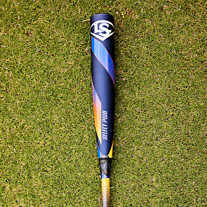 A 2025 Louisville Slugger Select PWR (-3) BBCOR Baseball Bat (WBL2967010) sits on the grass, its EXD Premium Alloy Barrel shining in the sunlight.