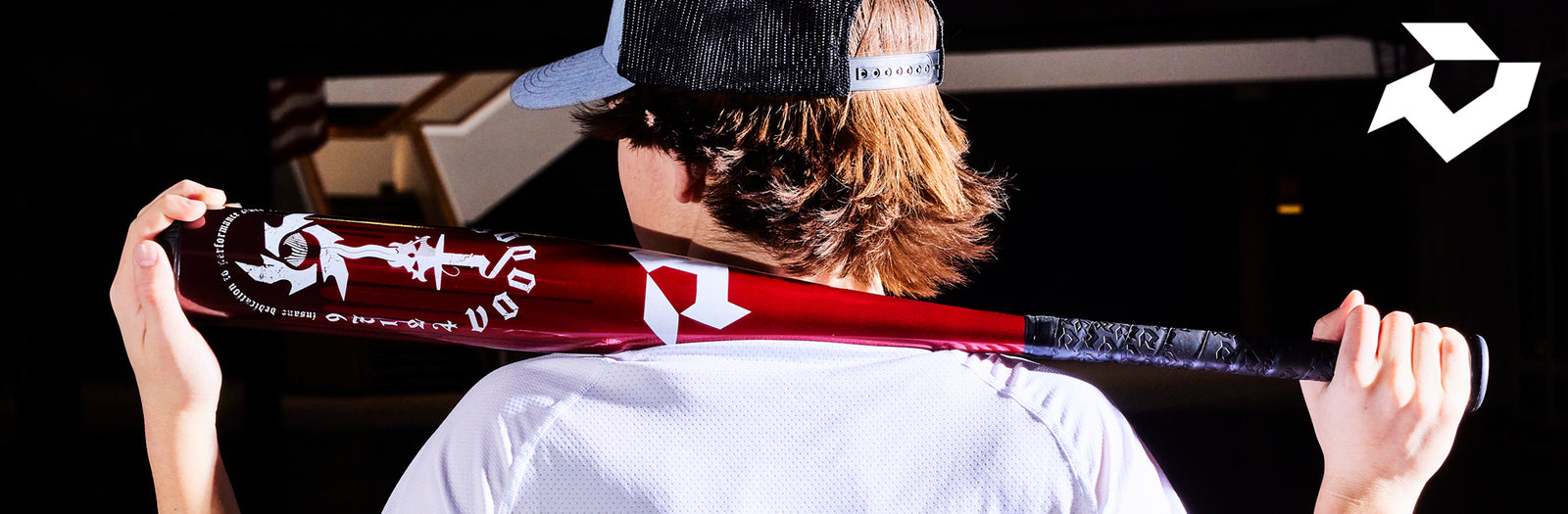 A person wearing a black cap and white shirt holds a red baseball bat with white graphics over their shoulders. A white geometric logo is visible in the top right corner.