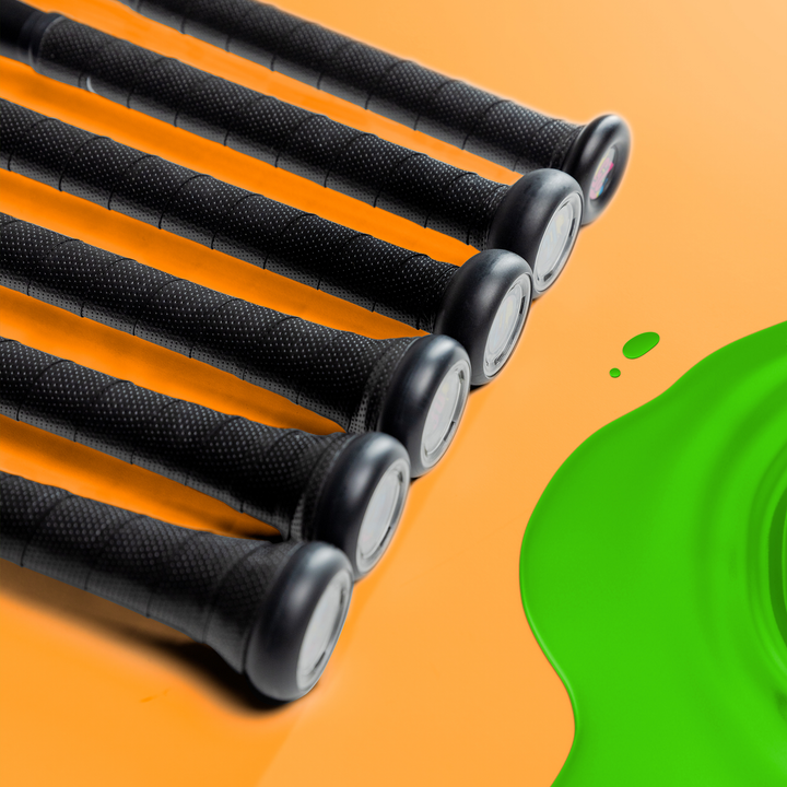 Six 2024 Victus Vibe (-8) 2 3/4" USSSA Baseball Bats from Victus are displayed diagonally on an orange surface, with a green liquid spill in the bottom right corner.