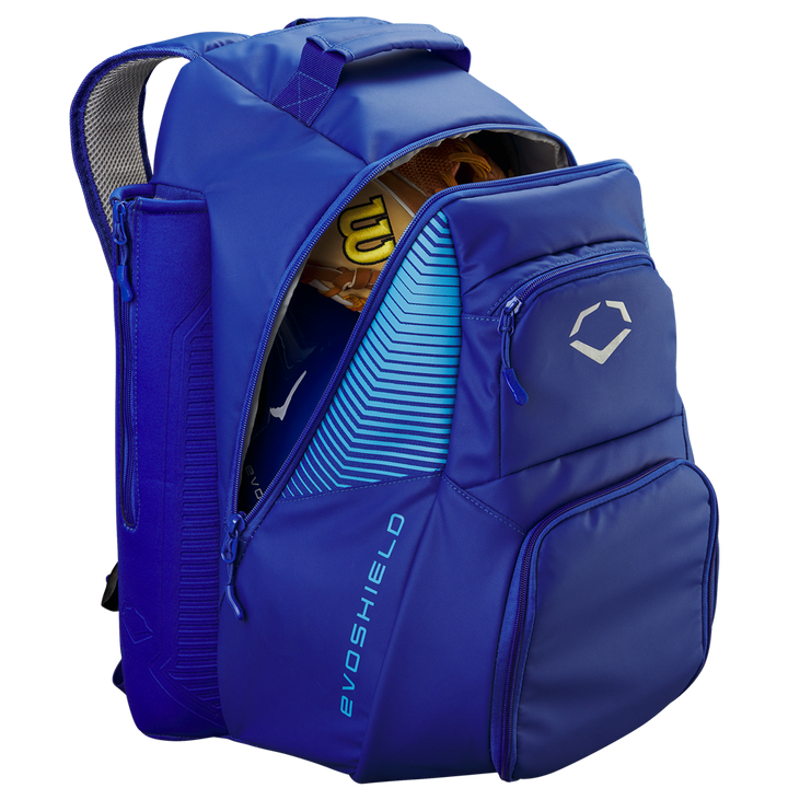 The EvoShield Tone Set Backpack: WB57304 in blue is shown unzipped with a yellow baseball glove inside. It features multiple compartments, bat sleeves, and displays the EvoShield logo and brand name on the front.