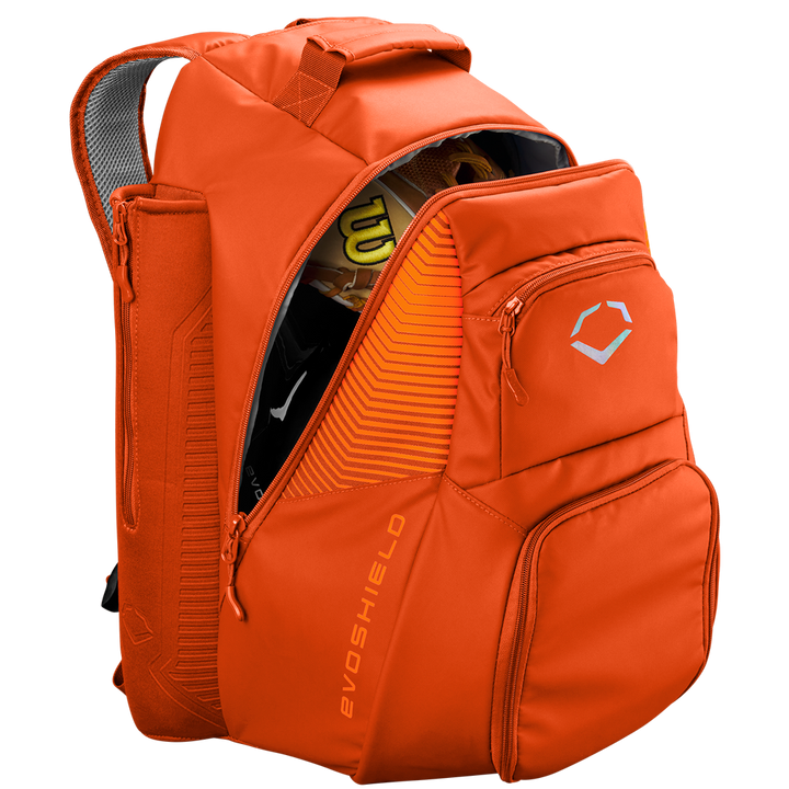 The EvoShield Tone Set Backpack (WB57304) by EvoShield is an orange, water-resistant backpack with multiple zippered compartments, bat sleeves, a top handle, padded straps, and sports gear inside like a yellow and black helmet.