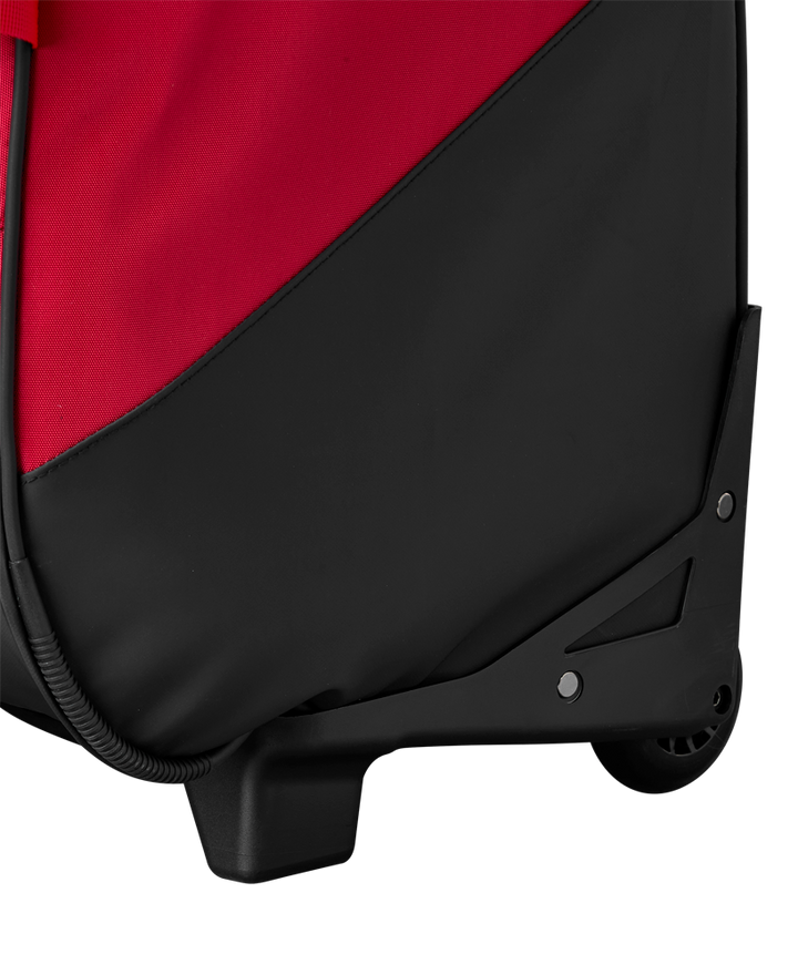 Close-up of the bottom corner of the EvoShield Takeover Wheeled Bag (WB57572) in red and black, showing the wheel, sturdy plastic base, and durable fabric material.