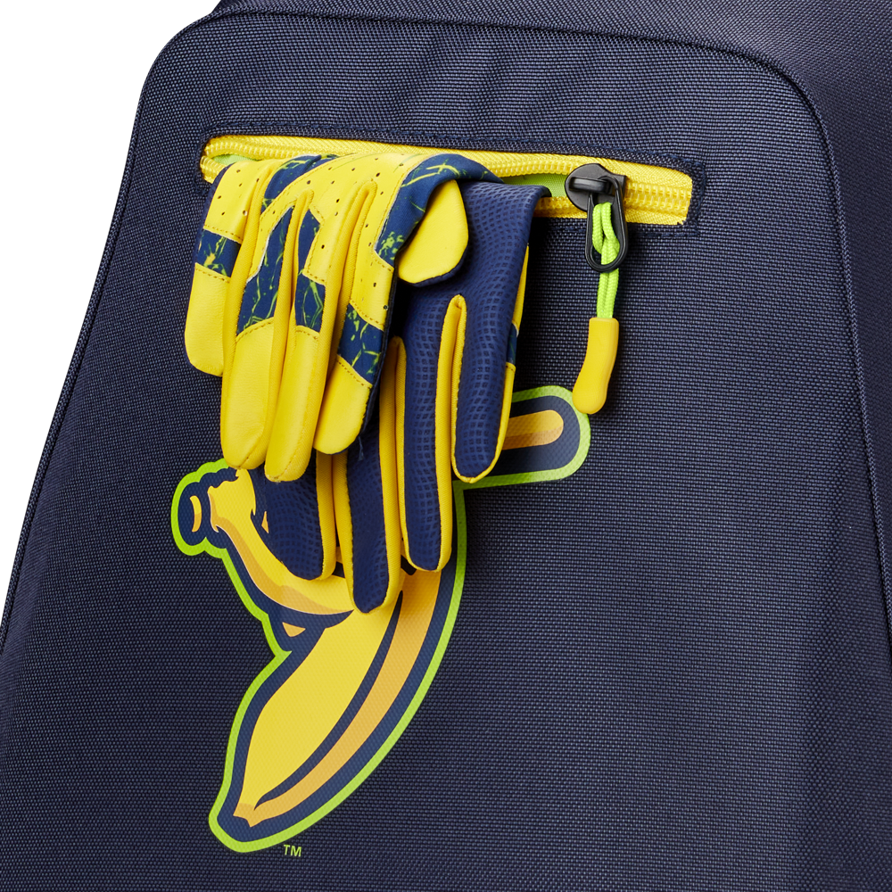 A pair of yellow and blue sports gloves is tucked into the pocket of a navy Louisville Slugger Savannah Bananas Powerized Stick Pack Backpack (WB57636), which features a graphic yellow banana.