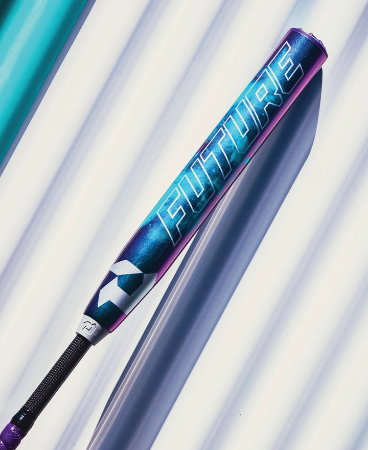 The 2026 DeMarini Future (-10) Fastpitch Softball Bat (WBD2674010), featuring a blue and purple gradient with bold white "FUTURE" lettering, rests on a white corrugated surface and offers a large sweet spot.