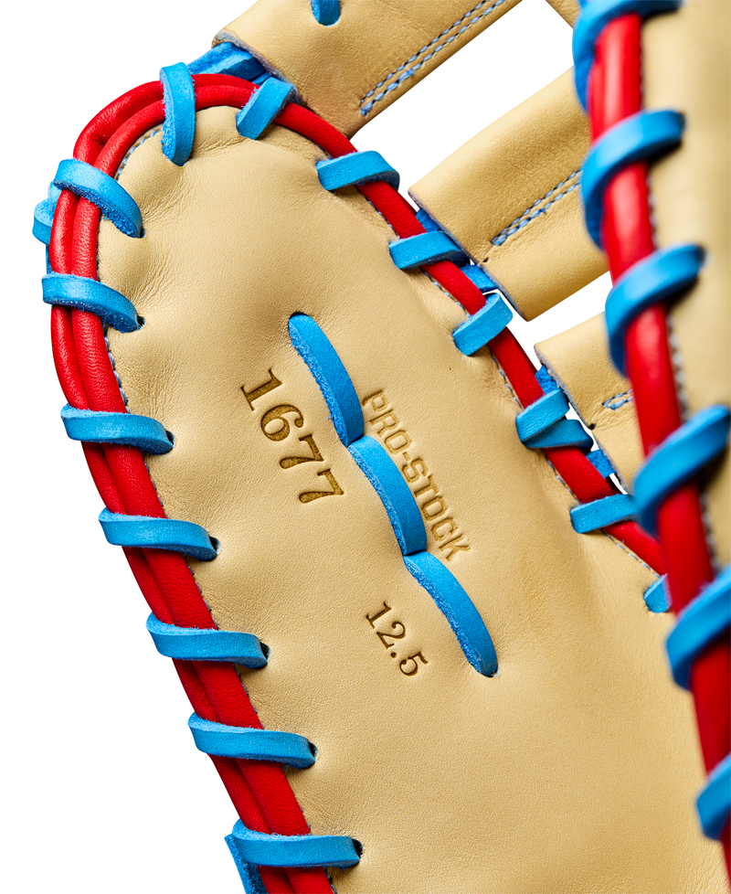 Close-up of the Wilson A2000 1677 12.5" First Base Mitt, featuring tan Pro Stock leather with blue and red lacing, and "1677," "PRO STOCK," and "12.5" stamped in gold on the palm. Model: WBW102753125.