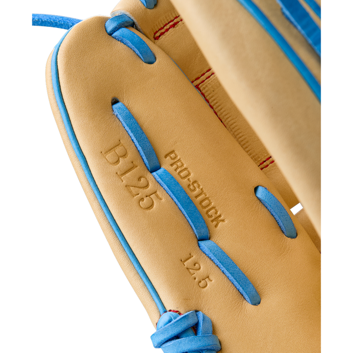 Close-up of the Wilson A2000 B125 12.5" Baseball Glove featuring tan Pro Stock leather, blue laces, and red stitching. "PRO-STOCK" and "12.5" are embossed on the glove. Model: WBW103220125, Summer 2025 release.