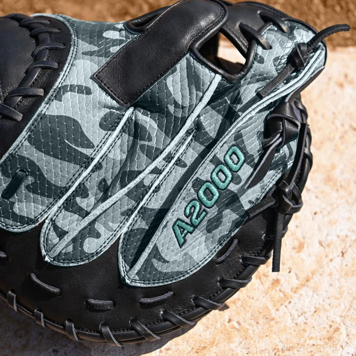 A Wilson A2000 AW28 34" Austin Wells Gameday Catcher's Mitt (WBW10349434) with camouflage leather and green stitching, shown close-up on a light, textured stone surface. Brand: Wilson.
