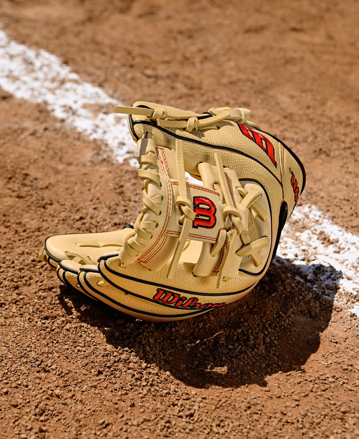 A Wilson A1000 PF11 11" Baseball Glove (WBW10395511) by Wilson rests open on the brown dirt near a white chalk line, ready for action on the baseball field.