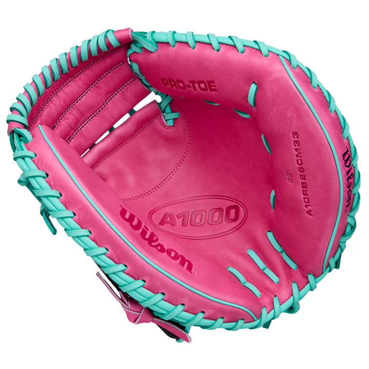 A Wilson A1000 CM33 33" Baseball Catcher's Mitt (WBW10396633) in pink with teal laces, seen from above to reveal the palm and interior branding. Crafted from full grain leather by Wilson.
