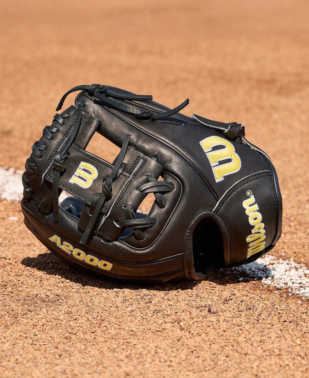 A Wilson A2000 1788 11.25" Baseball Glove (WBW1041051125) from Wilson, made with Pro Stock Leather, sits on a dirt field beside a white chalk baseline.
