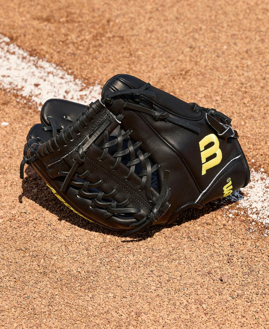 A Wilson A2000 1789 11.5" Baseball Glove (WBW104106115) with yellow lettering rests on the dirt near a white chalk baseline on the baseball field.