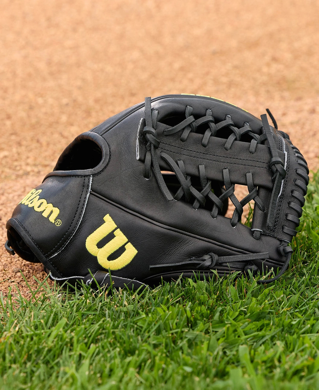 A Wilson A2000 1789 11.5" baseball glove (model WBW104106115) with yellow lettering lies on green grass near the infield, crafted from premium Pro Stock leather.