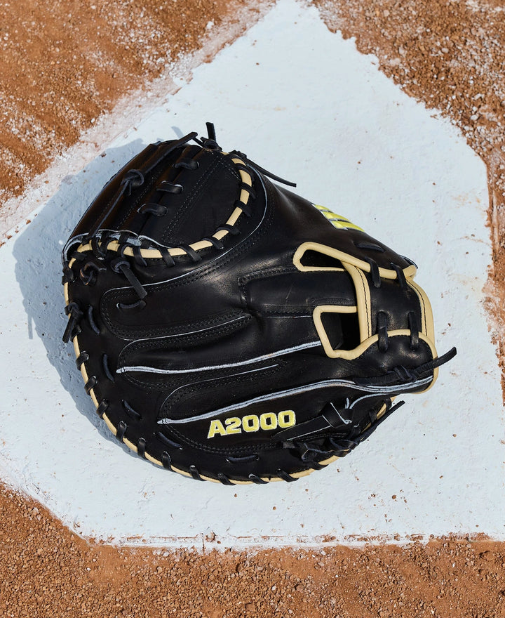 A Wilson A2000 1734 34" Baseball Catcher's Mitt (WBW10412834) with black leather and beige laces sits on home plate, highlighting its premium Pro Stock Leather and Wilson craftsmanship.