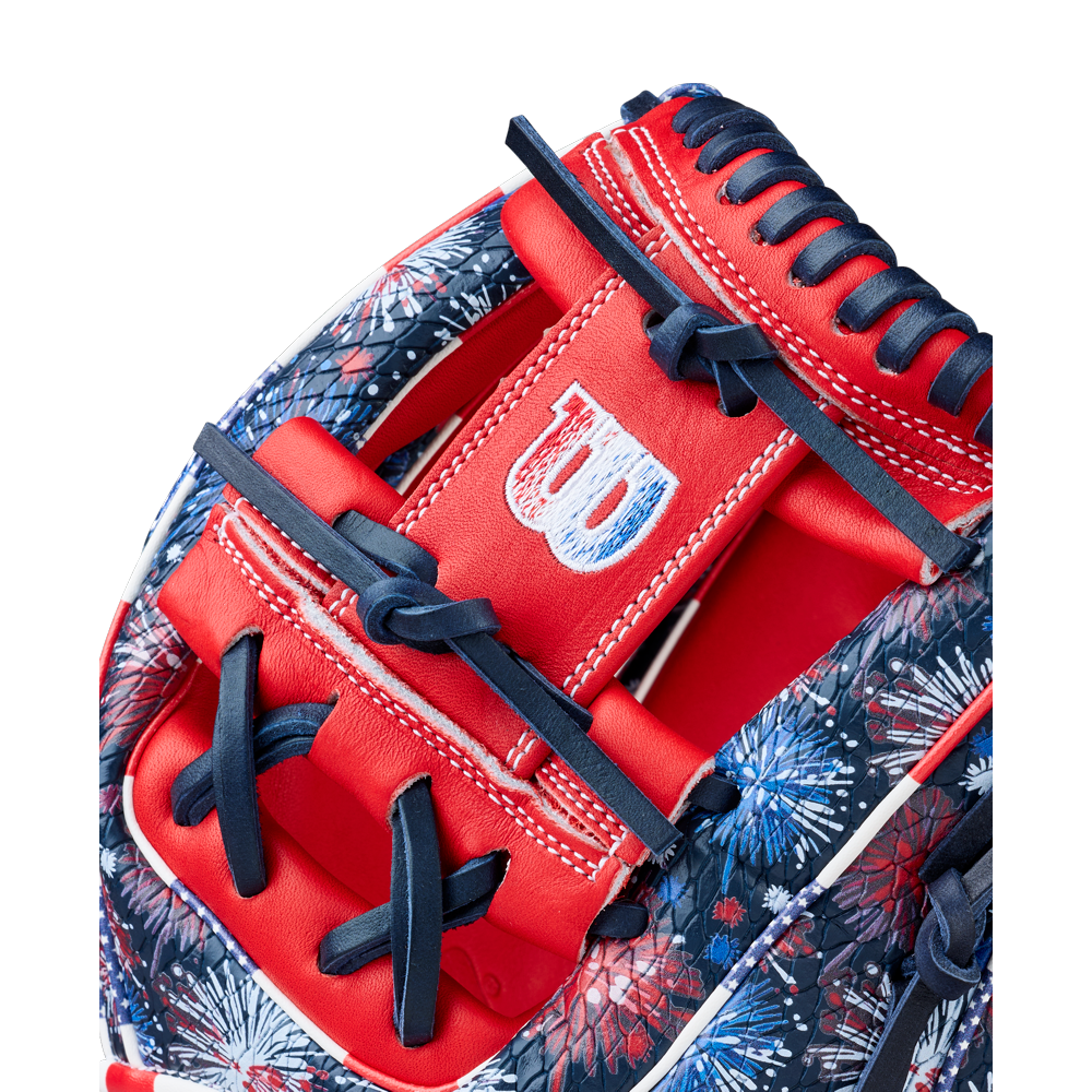 Close-up of the Wilson A2000 1975SS 11.75" Baseball Glove - GOTM July 2025, featuring red, white, and blue Pro Stock leather, navy laces, detailed stitching, the Wilson logo on the strap, and a vibrant fireworks pattern.