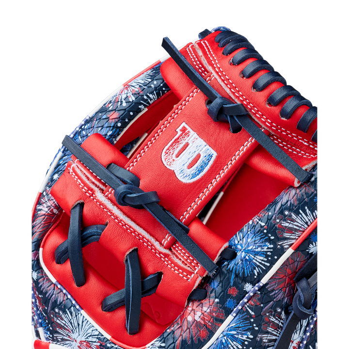 Close-up of the Wilson A2000 1975SS 11.75" Baseball Glove - GOTM July 2025, featuring red, white, and blue Pro Stock leather, navy laces, detailed stitching, the Wilson logo on the strap, and a vibrant fireworks pattern.