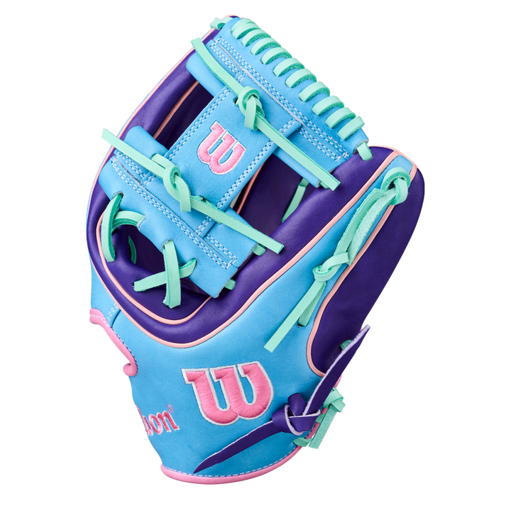 The Wilson A2K 1720 11.5" Baseball Glove (GOTM October 2025, WBW104220115) features blue, purple, and pink Pro Stock Select leather with teal laces and a pink Wilson logo on the wrist and thumb.