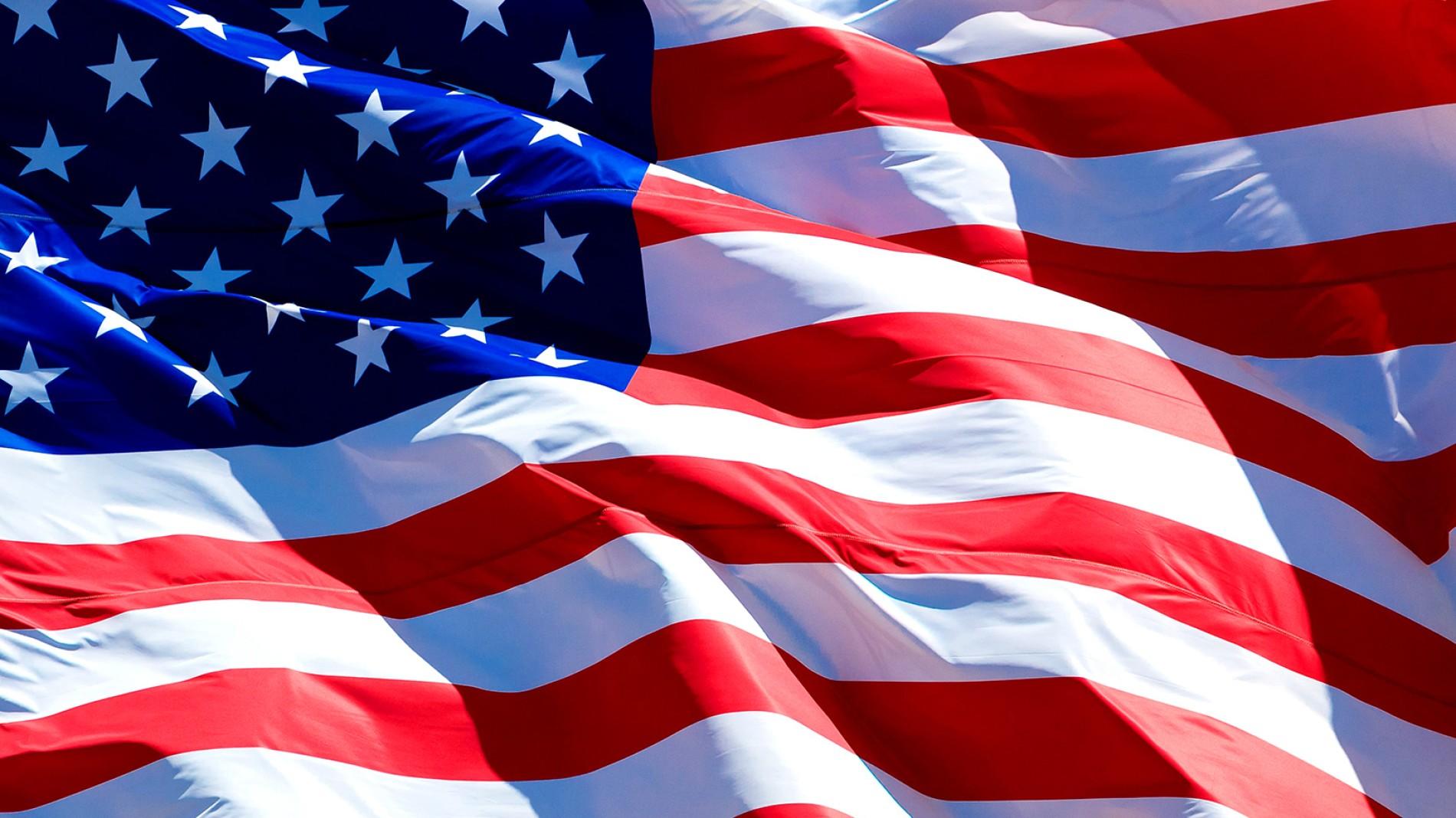 Close-up of the United States flag waving, showing red and white stripes with a blue field of white stars in the upper left corner.
