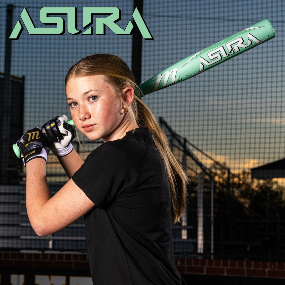 A young girl with a ponytail holds a green ASTRA baseball bat, ready to swing, on a baseball field at sunset. She wears black gloves and shirt; the ASTRA logo appears above her and on the bat.