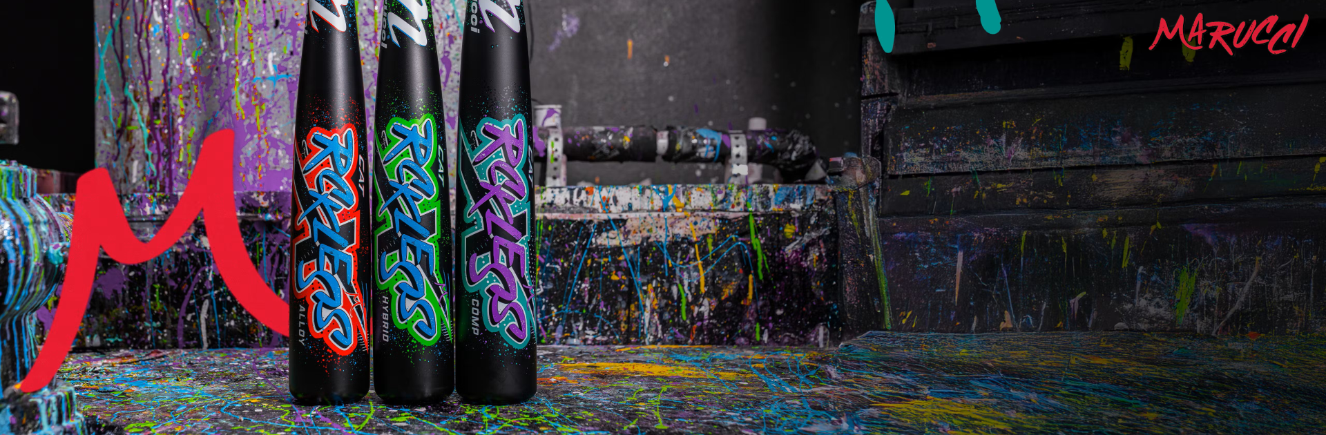 Three Marucci CATX baseball bats with colorful graffiti-style text stand upright in a splattered paint workshop. The red Marucci logo appears in the upper right and a large red M is drawn on the left side of the image.
