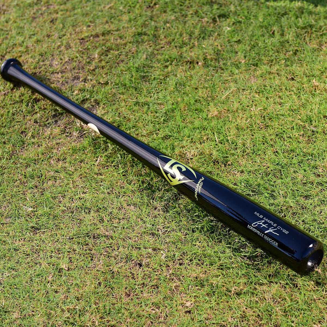 A Louisville Slugger MLB Prime Signature Series CY22 Christian Yelich Game Model Wood Baseball Bat (WBL2435010), featuring black wood with gold and white accents, rests on green grass.