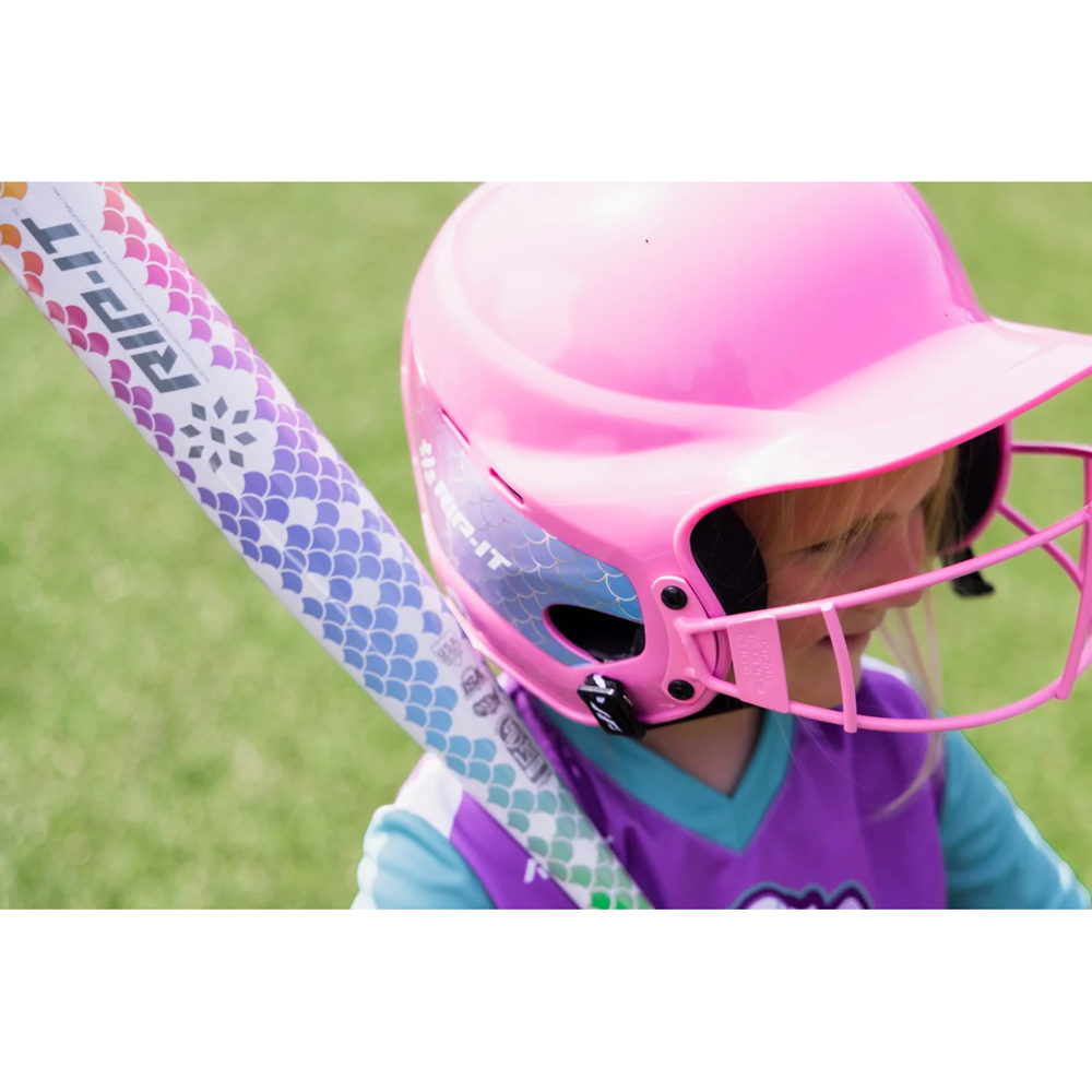 A young child in a bright pink helmet and purple sports uniform holds the Rip It 2022 Spark -12 Fastpitch Softball Bat (SRPK) on a grassy field.